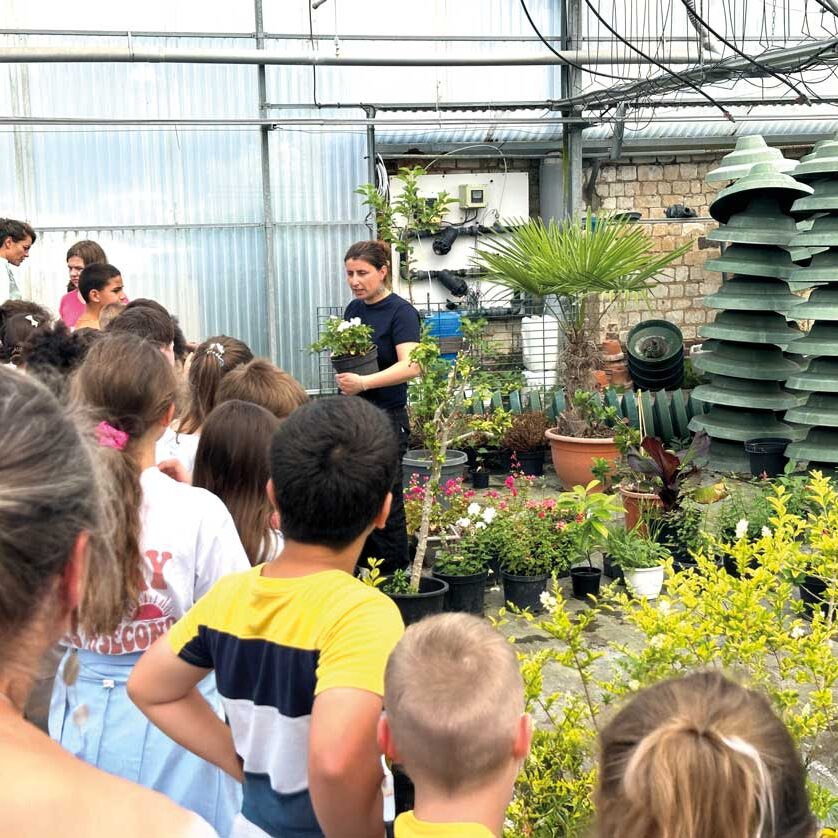 une agent des Espaces verts parle à des enfants avec une plante dans les mains